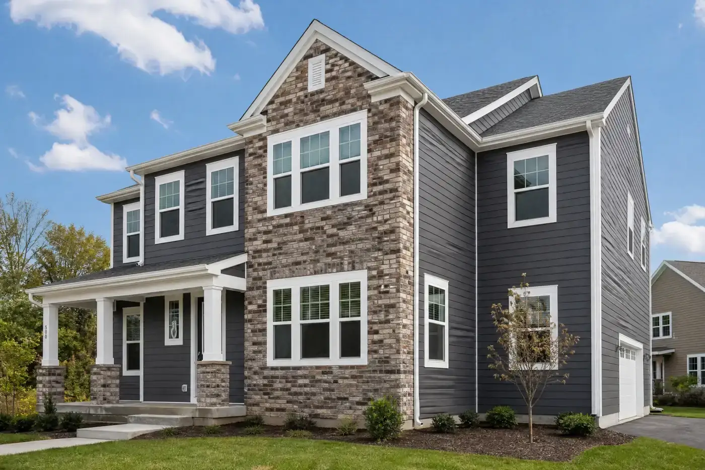 A multi-story home with dark gray siding and a protruding section featuring multiple windows that is covered in brown, gray, and white brick. The window frames, trim, and gutters on the home are white.