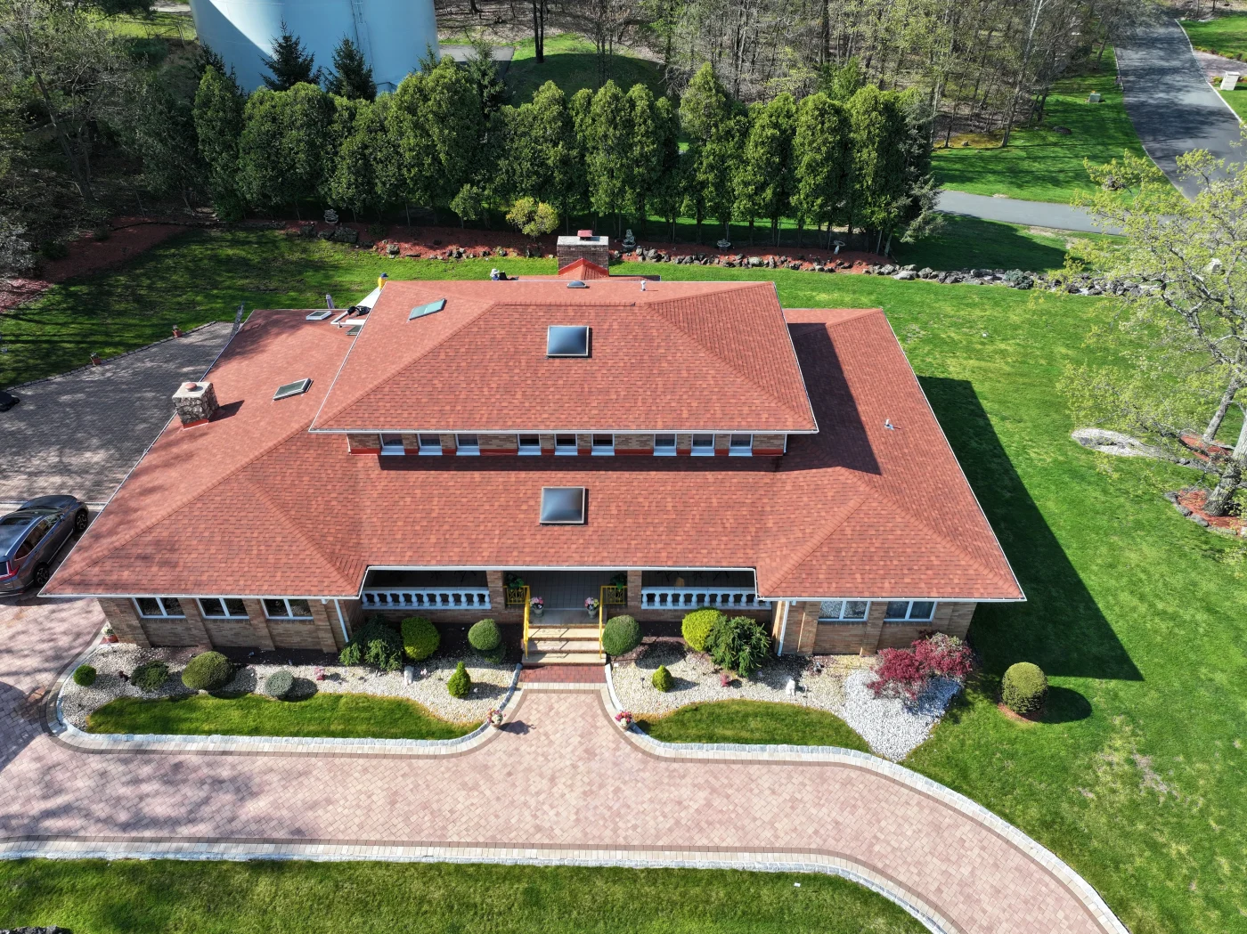 An aerial view captures a large multi-tiered residential home featuring a beautifully installed reddish-brown architectural shingle roof with skylights, showcasing the flawless craftsmanship of a trusted roofing contractor.